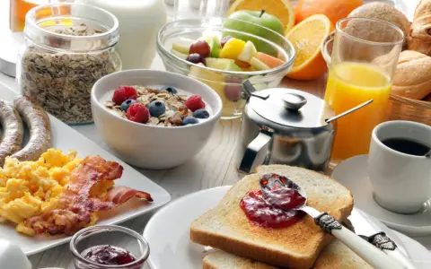 Deftiger Brunch in Schleswig-Holstein: Rührei, Speck, Würstchen, Müsli, Obst, Saft und Kaffee.