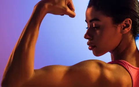 En kvinna flexar sin biceps, en demonstration av styrka och i muskelminnet.