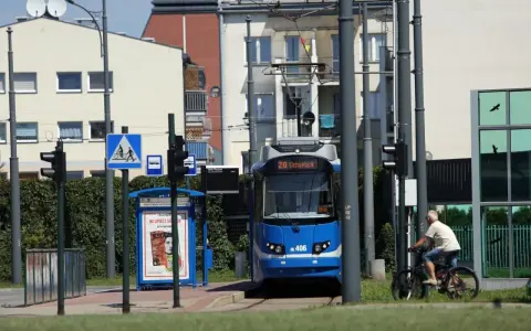 Niebieski tramwaj na przystanku w Krakowie, obok rowerzysta i znaki drogowe.