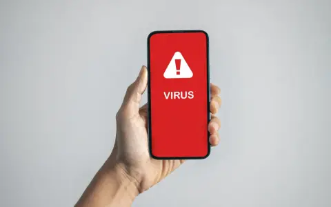 En hand håller upp en mobil med en röd skärm som varnar: "VIRUS".