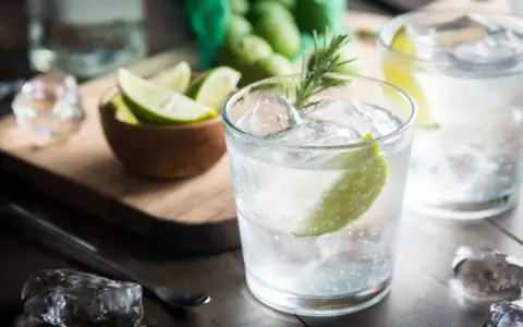 Kto pije gin z tonikiem? Orzeźwiający drink z lodem, limonką i rozmarynem, gotowy do degustacji.