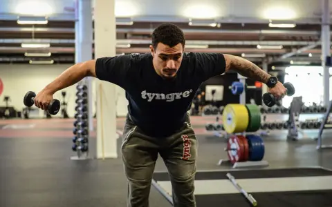 Man tränar baksida axlar med hantlar på gym.