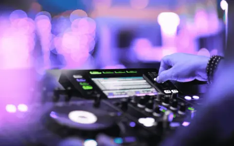 Mano su mixer, luci viola e rosa sfocate, creando l'atmosfera perfetta per la musica tech house.
