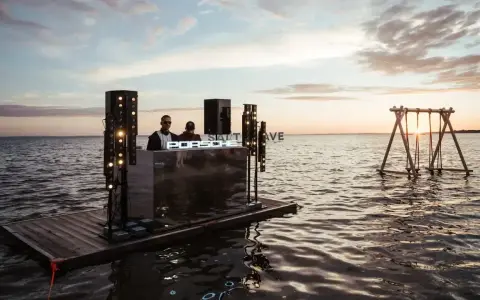 DJ na wodnej platformie podczas Salt Wave Festival. W tle huśtawka na jeziorze o zachodzie słońca.