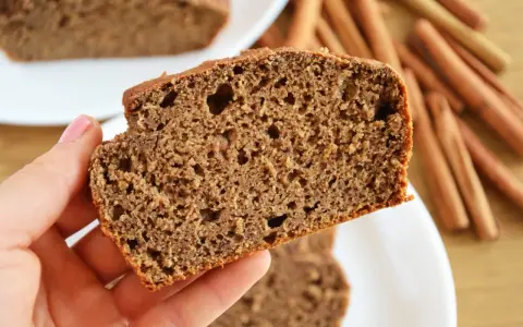Kawałek wilgotnego chlebka bananowego bez cukru, z widocznymi kawałkami banana i cynamonem w tle.