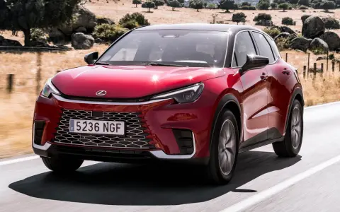 El Lexus LBX rojo brillante se desplaza por una carretera rural, con un paisaje seco y rocoso de fondo.