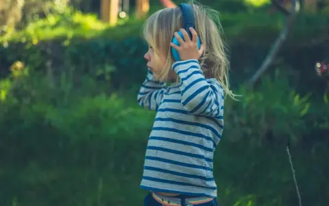 Ein Kind mit Kopfhörern im Freien, das die Welt der Klänge entdeckt. Diese Szene zeigt die Reizoffenheit bei Kindern, die sich neugierig auf neue Erfahrungen einlassen.