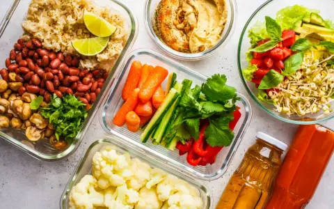 Gotowe pojemniki z jedzeniem na biwak bez gotowania: ryż z fasolą i pieczarkami, warzywa pokrojone w słupki, kalafior, sałatka z pomidorami i awokado, hummus i napoje.