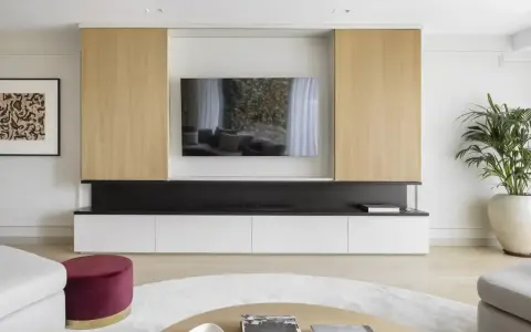 Un moderno mueble de salón con una gran televisión para poner la tele en medio del salón. Destacan los paneles de madera clara y los cajones blancos.