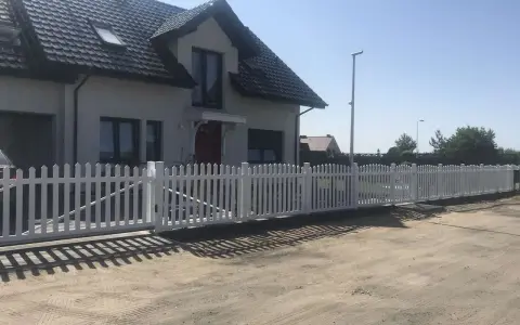 Biały płotek ogrodowy zrób to sam, idealnie otacza dom. Wygląda jak nowy, dodaje uroku posesji.