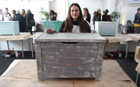 Una mujer muestra un baúl pintado a la tiza con un acabado desgastado. Otros baúles decorados se ven en el fondo.