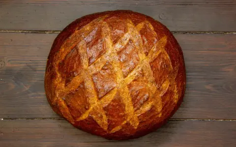 Ein **freigeschobenes Brot** mit knuspriger Kruste und Rautenmuster liegt auf dunklem Holz.