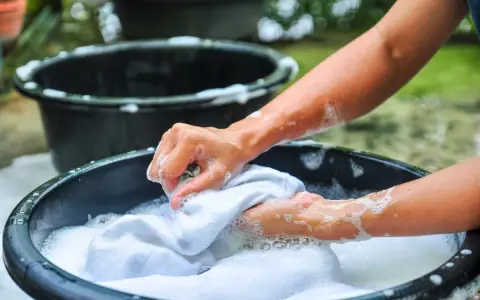 Manos lavando ropa blanca a mano en una tina con espuma, un método tradicional que explica qué significa lavado a mano en lavadora.