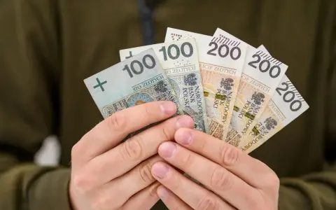 Dłonie trzymają polskie banknoty: 100 i 200 zł. To symbol nagrody za pracę, jak 800 plus tylko dla pracujących.