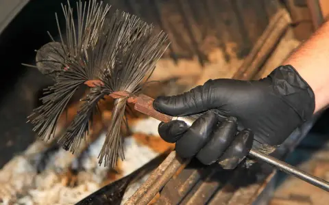 Main d'un ramoneur tenant une brosse pour cheminée. Le ramonage est essentiel pour l'assurance.