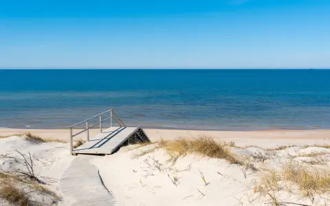 Drewniane schody prowadzące na piaszczystą plażę nad spokojnym Bałtykiem.