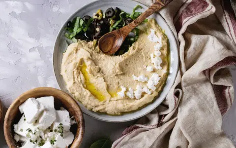 Pyszna pasta z ciecierzycy z fetą, oliwkami i ziołami, podana z serem feta w drewnianej misce.