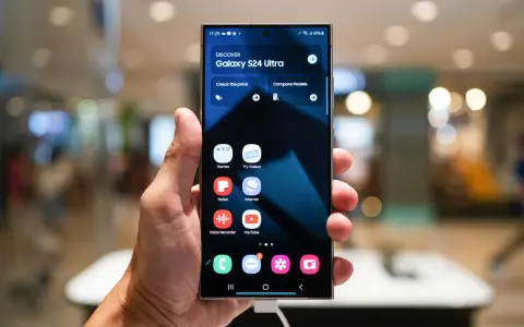 Dłoń trzyma smartfon z interfejsem One UI 6, prezentującym ekran startowy Galaxy S24 Ultra z ikonami aplikacji.