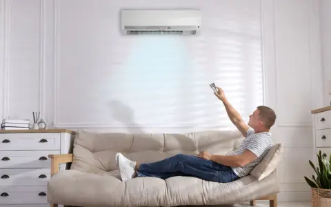 Hombre relajado en el sofá, ajustando el aire acondicionado para dormir cómodamente.