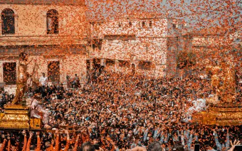 Folla festante sotto una pioggia di coriandoli arancioni, mentre si celebra cosa si festeggia a Pasqua con una processione solenne.