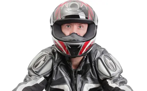 Occhi spalancati dietro un casco stretto, pronto per la corsa. La tuta in pelle grigia e nera completa il look da motociclista.