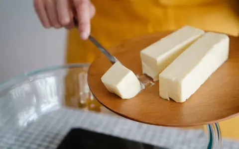 Ein Stück Butter wird mit einem Messer von einem Holzbrett gehoben, bereit für die Zubereitung von Butterschmalz.