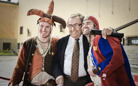 Jonas Elgh skrattar med två män i medeltida kläder. En har en narrmössa, den andra en röd och blå dräkt.