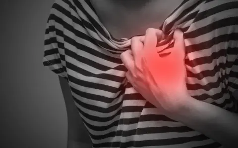 Brustschmerz, ein mögliches Symptom von zu viel Koffein. Eine Hand greift schmerzhaft zur Brust.