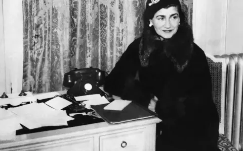Coco Chanel, icona di stile, al suo scrittoio. La sua storia è fatta di eleganza e innovazione.
