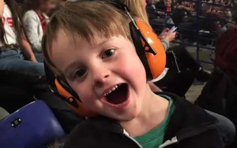 Un jeune garçon de 3 ans, avec un bouchon oreille enfant 3 ans, sourit à pleines dents, prêt pour le spectacle.