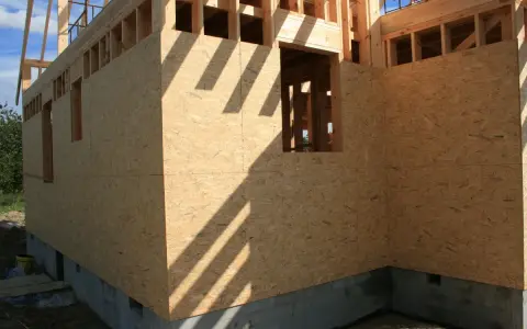 Budowa domu, ściany zewnętrzne z płyt OSB, widoczne okna i fundament.