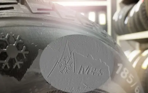 Zbliżenie na bieżnik opony z oznaczeniem M+S i symbolem płatka śniegu, sugerujące opony całoroczne lub zimowe.
