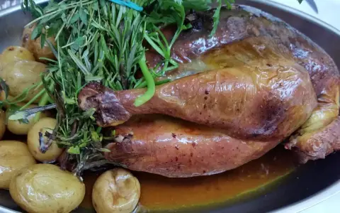 Pollo de Bresse asado, dorado y jugoso, acompañado de patatas pequeñas y hierbas frescas.