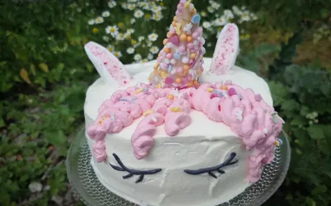 En förtrollande unicorn tårta med rosa glasstrut-liknande horn, dekorerad med strössel och blommor i bakgrunden.