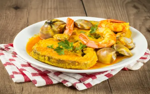 Plato de comida asturiana con un trozo de pescado, gambas y almejas en salsa.