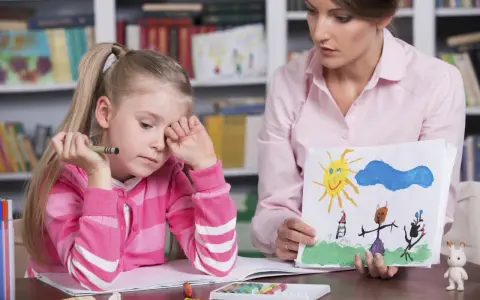 Dziewczynka z kredką w dłoni, smutna, podczas sesji socjoterapii. Terapeuta pokazuje jej rysunek.