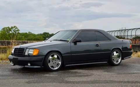 Ciemnoszary Mercedes "Hammer" coupe z przyciemnianymi szybami i chromowanymi felgami stoi na mokrej drodze.