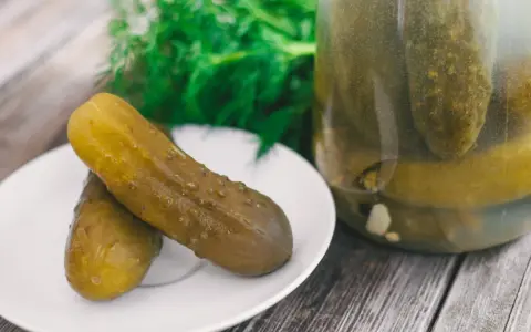 Dwa ogórki kiszone na talerzyku, obok słoik pełen kiszonków. Zastanawiasz się, dlaczego ogórki kiszone są puste w środku? To proces fermentacji!