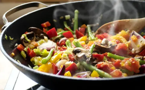 Un delicioso salteado de verduras humeante en un wok, con pimientos, judías verdes, champiñones y cebolla morada.