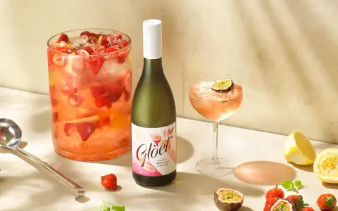 En stor bålskål fylld med jordgubbar och is, en flaska vitt vin och en cocktail med passionsfrukt. Perfekt för en somrig drink med vitt vin.
