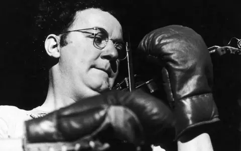 Coluche, lunettes rondes, gants de boxe, prêt à en découdre avec le racisme.