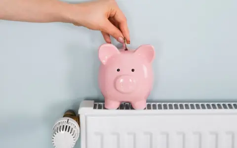 Mano inserta moneda en hucha rosa sobre radiador blanco. Ahorrando energía cuando se apaga la calefacción central.