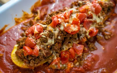 Herzhafte zucchini schiffchen gefüllt mit Hackfleisch, Tomaten und Käse, in einer aromatischen Tomatensauce.