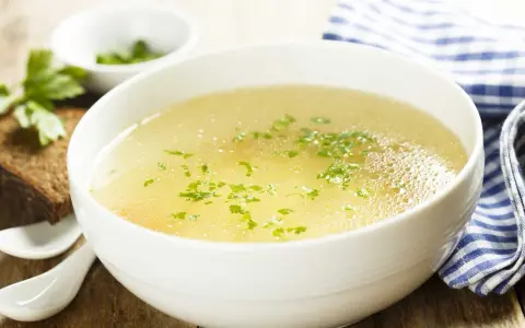 Aromaticzny rosół z perliczki, ozdobiony natką pietruszki, podany z kromką chleba. Idealny na chłodne dni.