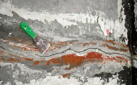 Espátula verde sobre pared agrietada con restos de pintura, como si se estuviera retirando el grout.