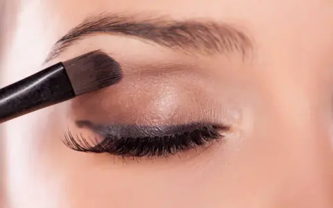 Application d'un fard à paupières marron pour un regard smoky intense.