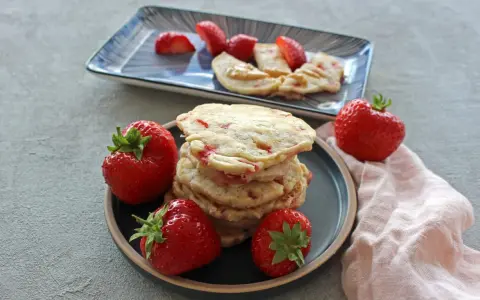 Ein Stapel Erdbeer-Pancakes mit frischen Erdbeeren auf einem Teller. Ein weiterer Teller im Hintergrund zeigt geschnittene Erdbeeren und Pancakes mit Erdnussbutter.