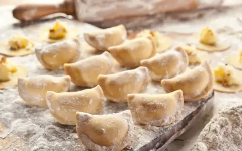 Gotujesz pierogi? Zobacz, jaka mąka do pierogów będzie najlepsza! Na zdjęciu świeżo lepione pierogi, wałek i rozsypana mąka.