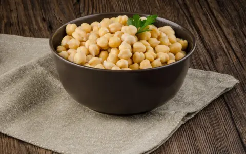 Schüssel mit Kichererbsen aus der Dose, bereit zum direkten Essen. Ein Hauch Petersilie und eine Knoblauchzehe im Hintergrund.