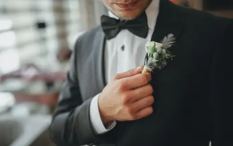 Mężczyzna poprawia butonierkę w eleganckim, czarnym garniturze.